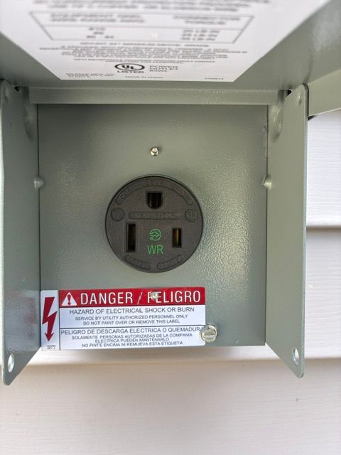 Open electrical outlet inside a metal box with a red danger warning label