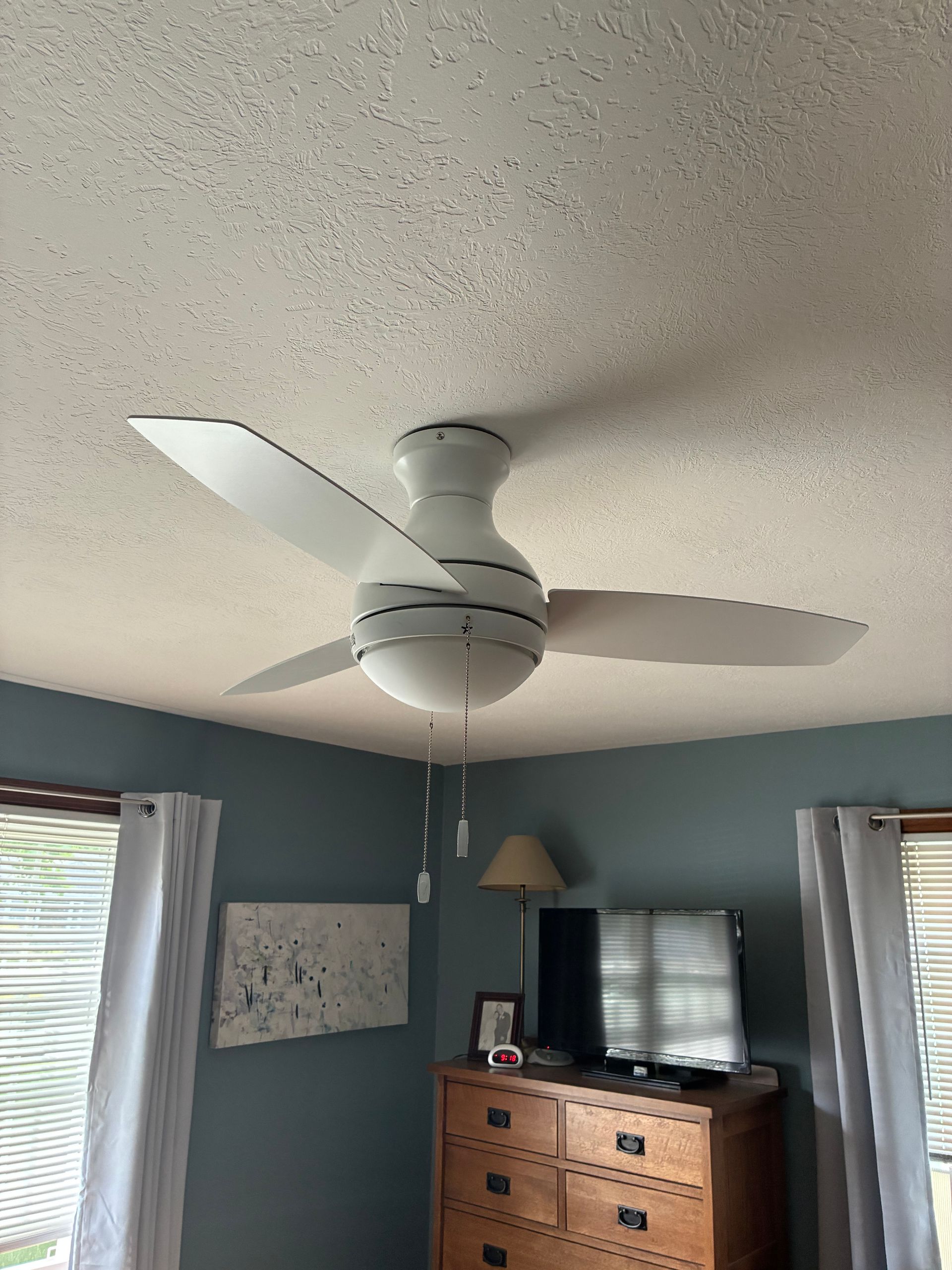 Ceiling fan in a blue bedroom with a dresser, TV, and window blinds