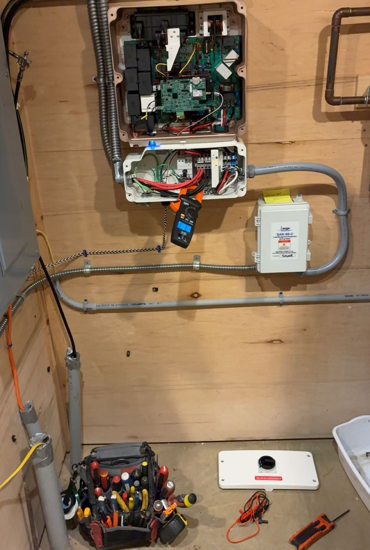 Open electrical panel with exposed wiring and tools on a wooden wall in a work area