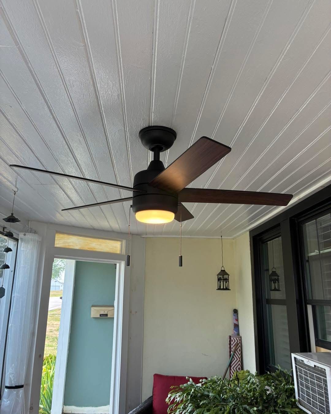 Covered porch with black ceiling fan, white paneled ceiling, and light blue door in the background