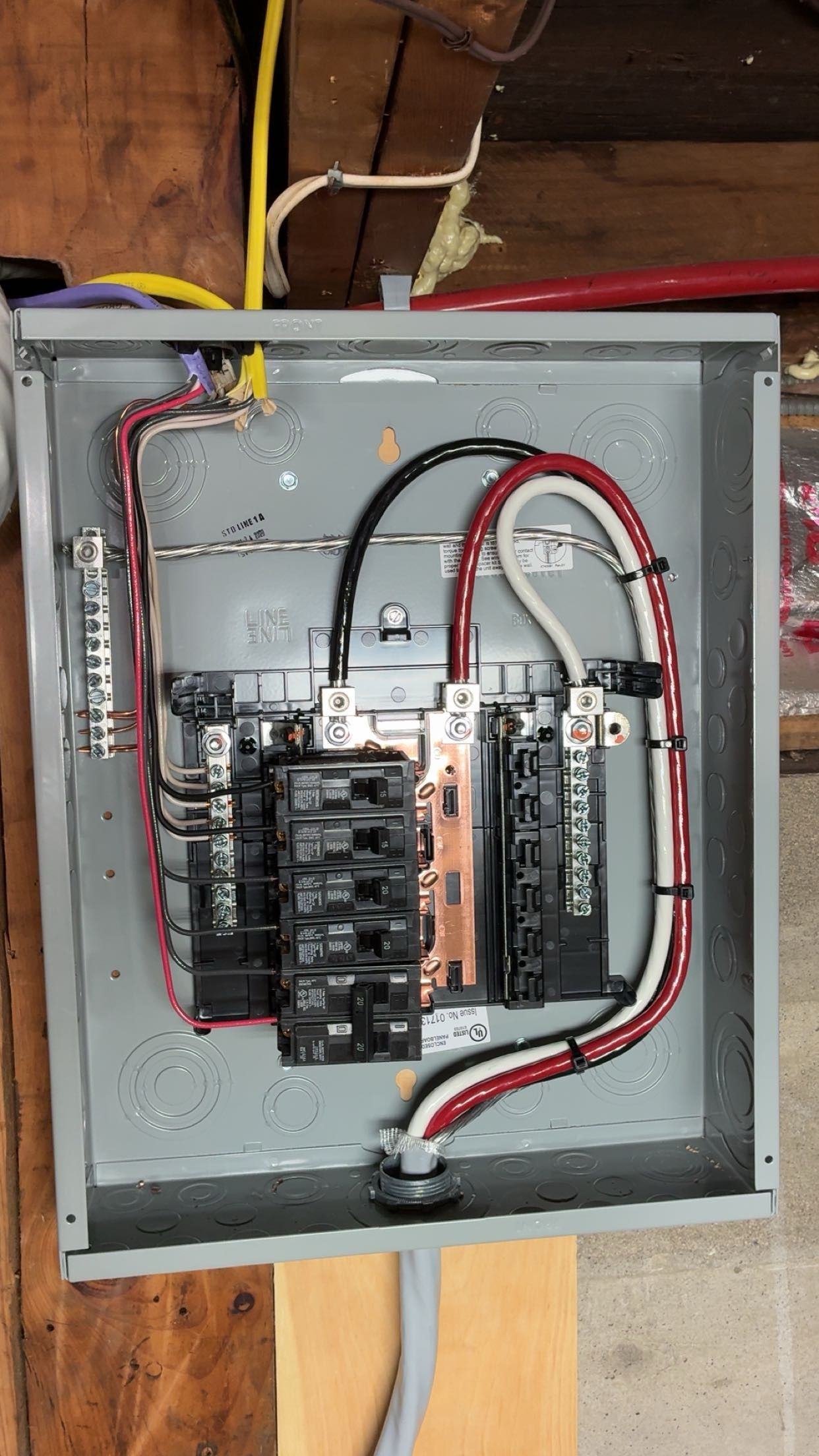 Open electrical breaker panel with wiring, red and black cables, and exposed components on a gray metal box.
