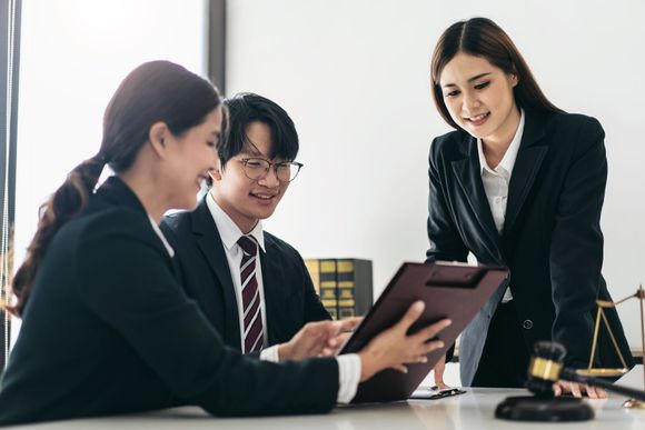 Three coworkers in business attire discussing a tablet during a meeting in a bright office