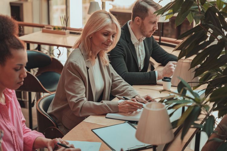 People seated at a table in a bright office, writing and working on documents and laptops