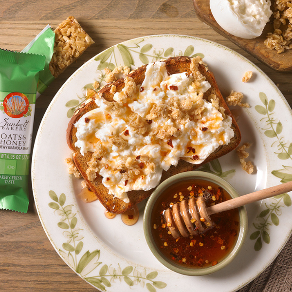 toast topped with granola bits, burrata cheese and hot honey on a white plate