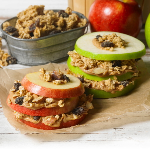 apple rings layered with granola and nut butter on brown parchment paper with apples in the background