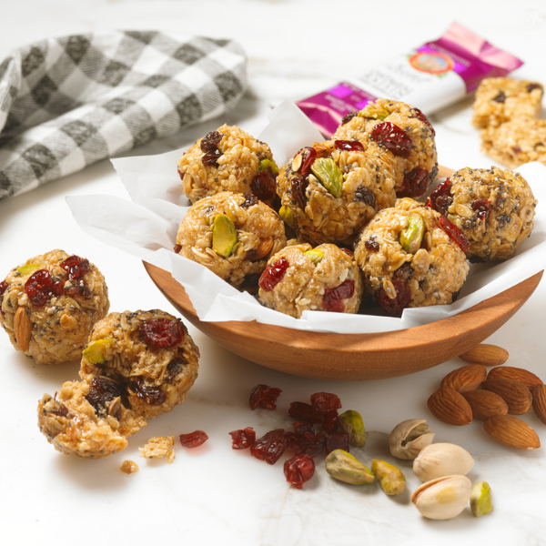granola balls made of nut butter, raisins and pistachios in a wooden bowl on a white background