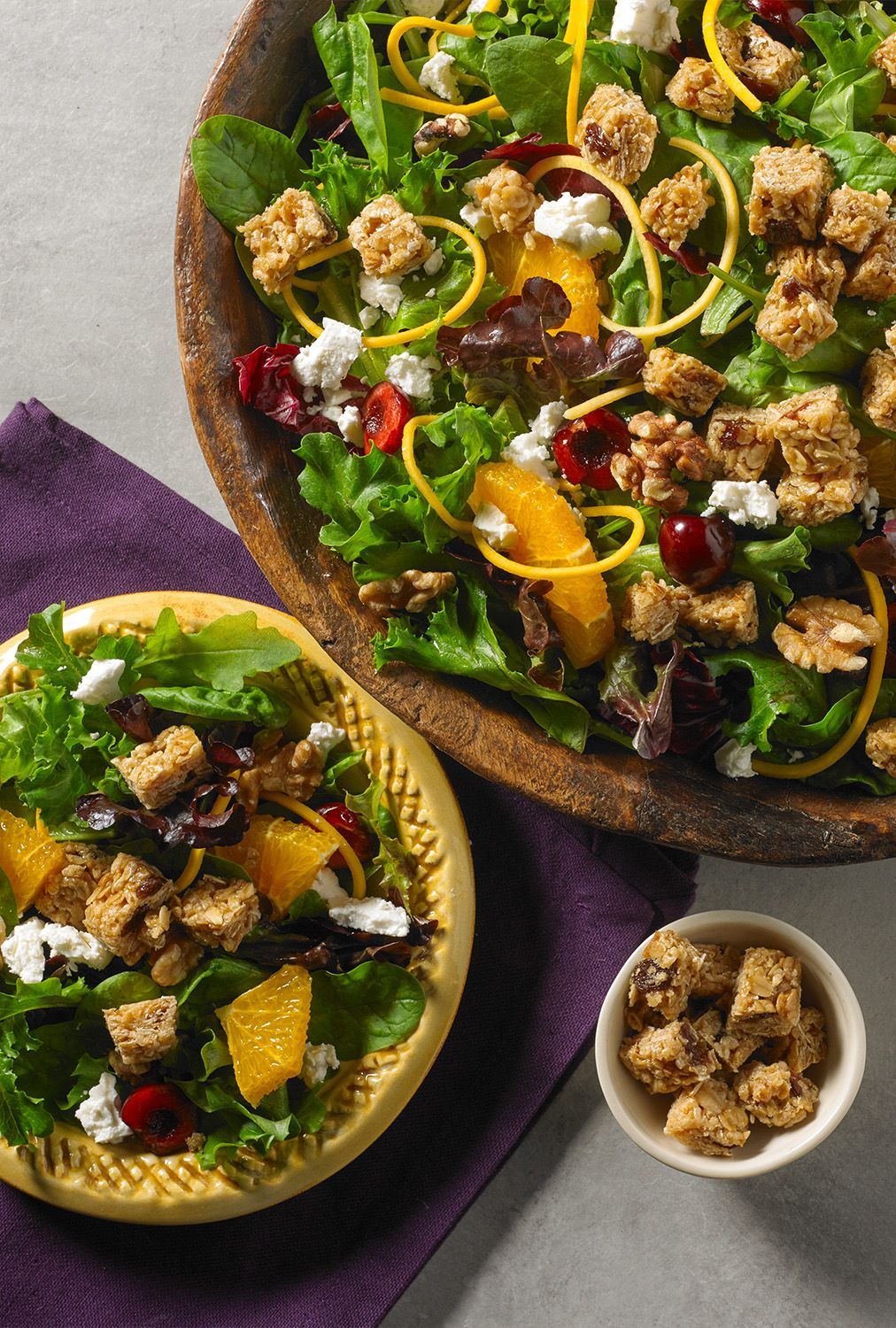 salad topped with granola bars chunks, cheese, cherries, oranges and other salad toppings in wooden bowl