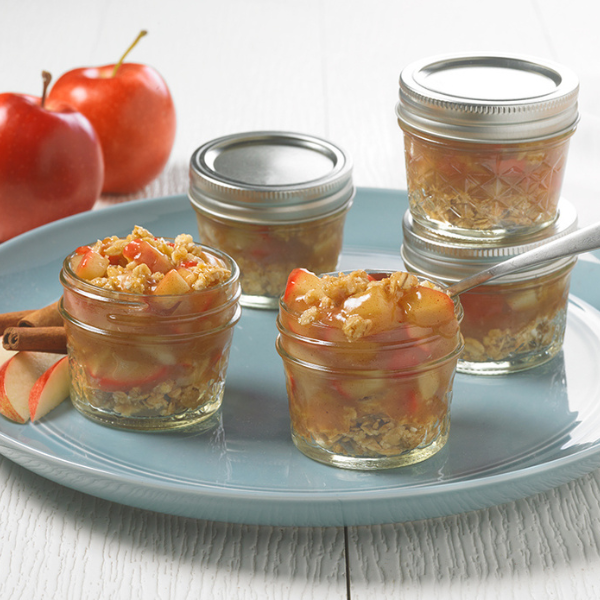 apple crisps in mini mason jars on a teal plate with apples in the background