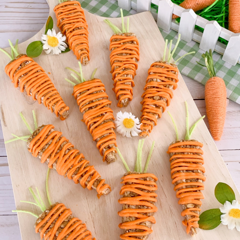 granola bars shaped and decorated like carrots for spring on a wooden board with green gingham and flowers