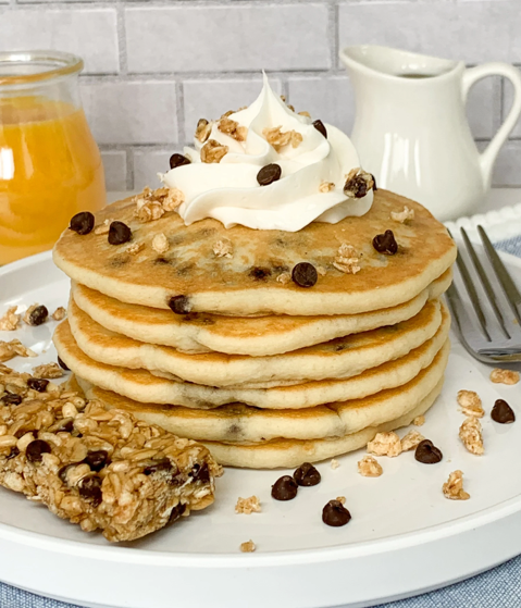 chocolate chip pancakes topped with granola and chocolate chips and whipped cream