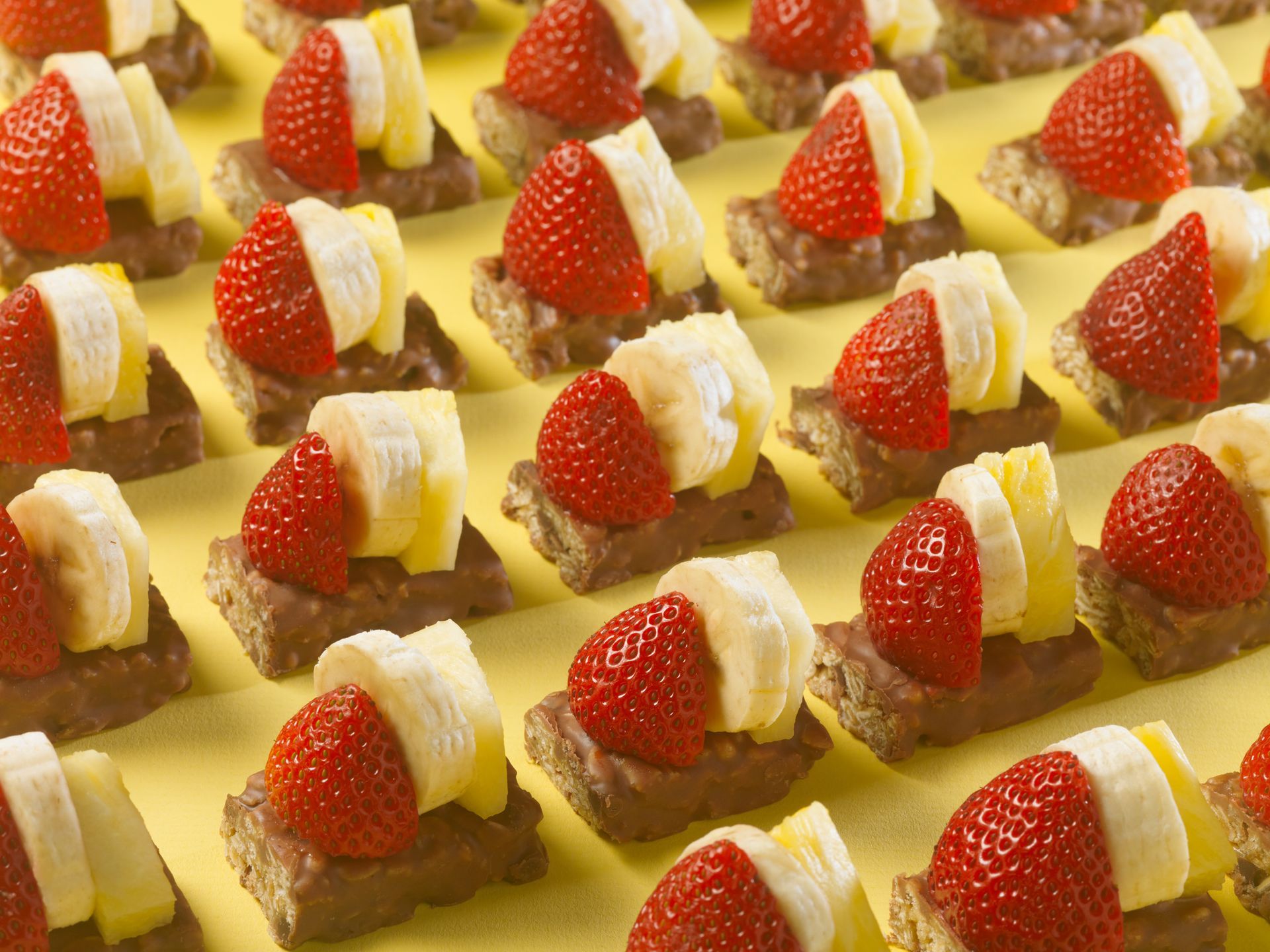fudge dipped bars cut in half and topped with strawberries, pineapple and banana slices on a yellow background