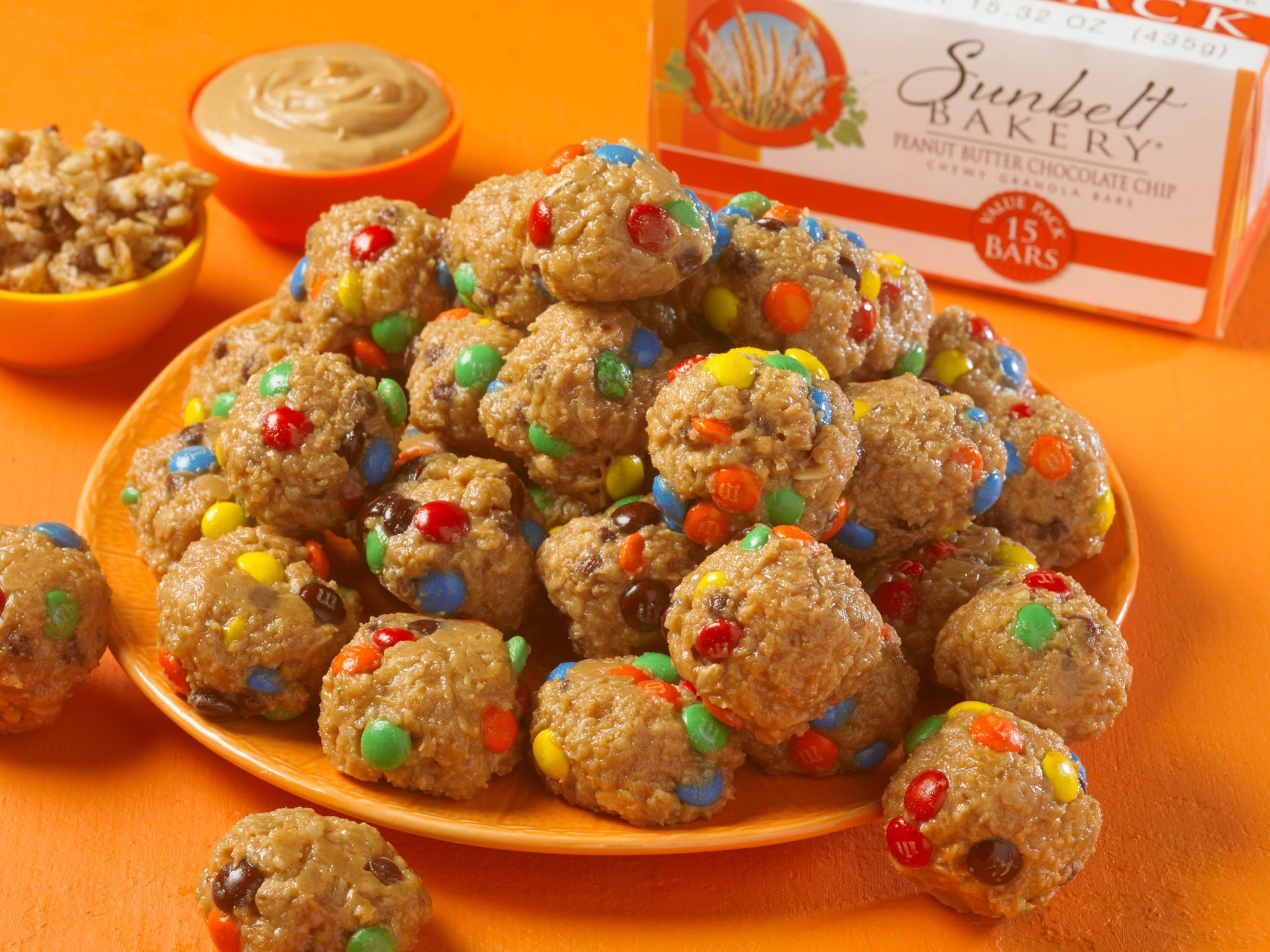 granola balls made of peanut butter and chocolate candies on an orange plate sitting on an orange background
