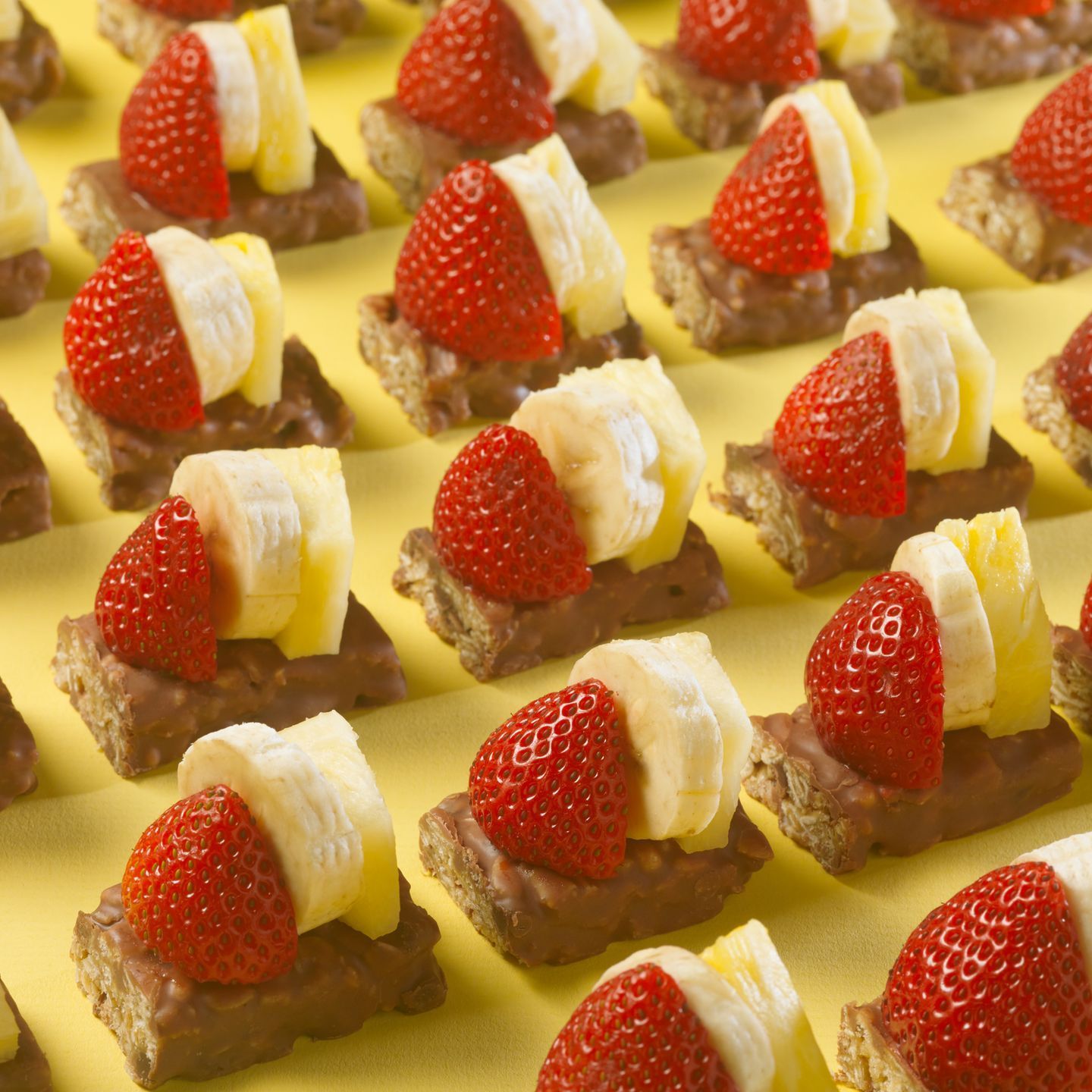 fudge dipped bars cut in half and topped with strawberries, pineapple and banana slices on a yellow background