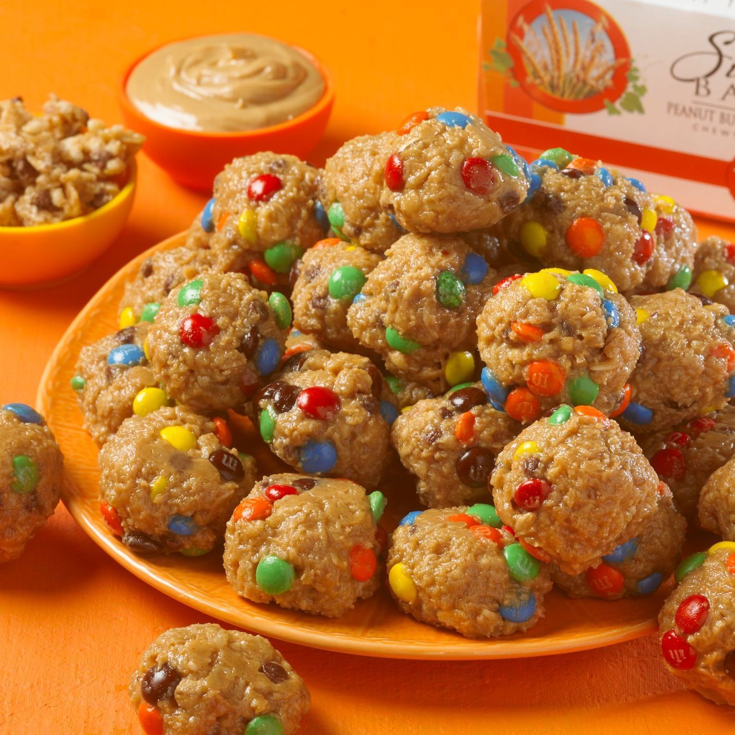 granola balls made of peanut butter and chocolate candies on an orange plate sitting on an orange background