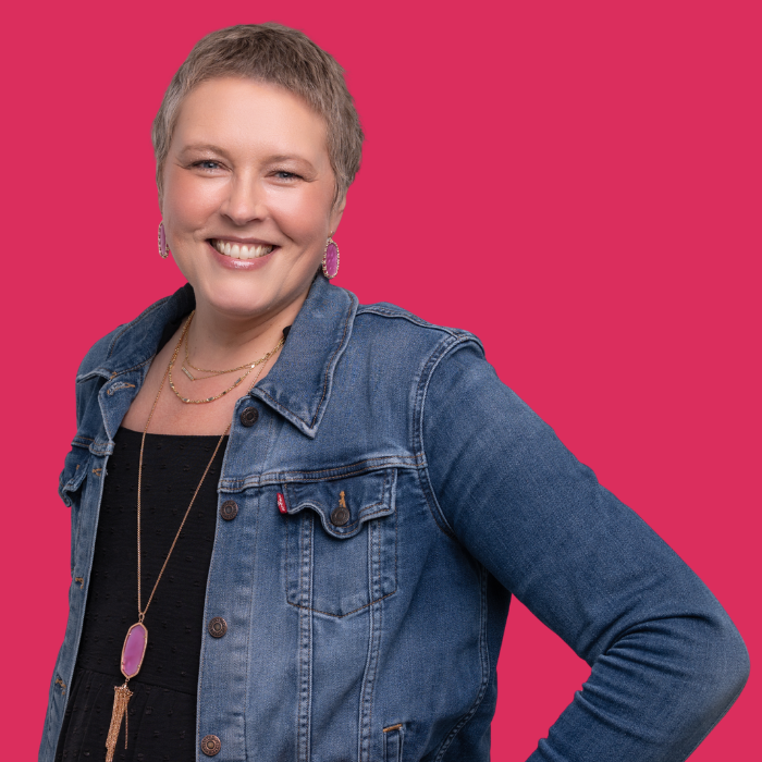 Smiling person in a denim jacket against a bright pink background