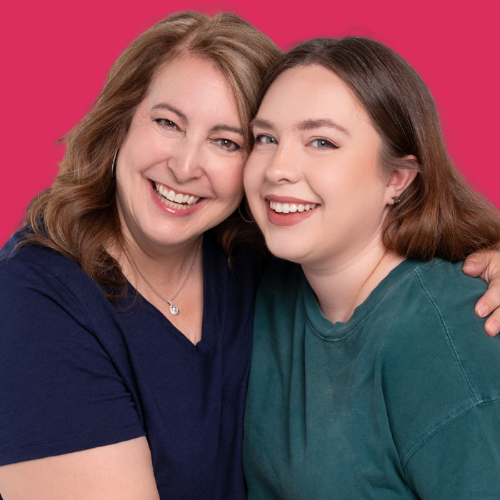 Two smiling women posing closely against a bright pink background