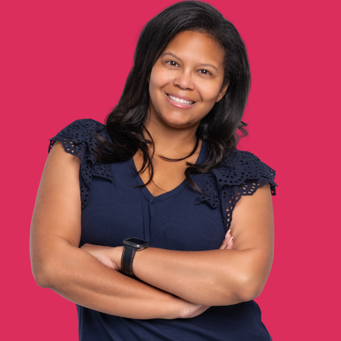 Smiling woman with crossed arms in a navy top against a bright pink background