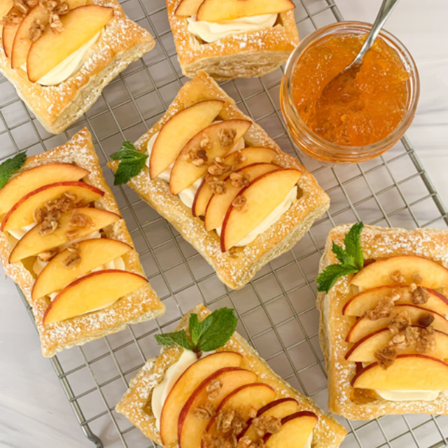 puff pastries on a cooling rack with sliced peaches, mint and granola crumble by a jar of peach preserves
