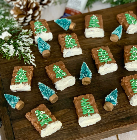 fudge dipped granola bar halves decorated with white icing and a tree for winter on a wooden board