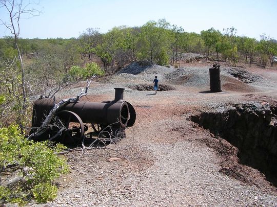test acknowledgement A man is standing in the middle of a dirt road next to a pile of pipes.