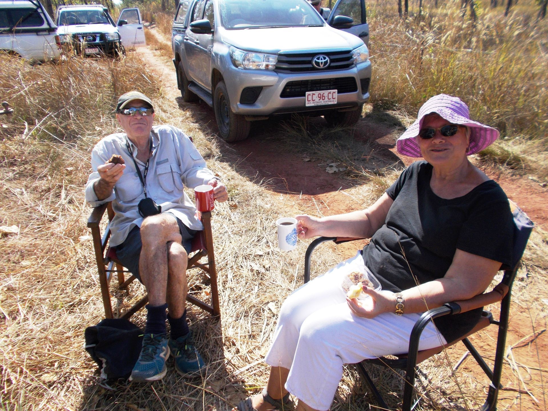 A man and a woman are sitting in chairs on a dirt road.