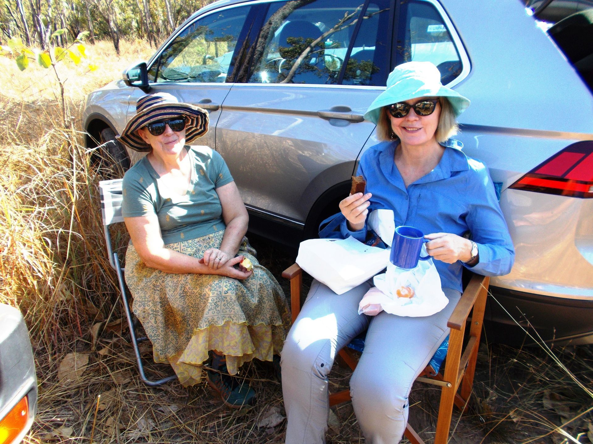 Two women are sitting next to each other in front of a car