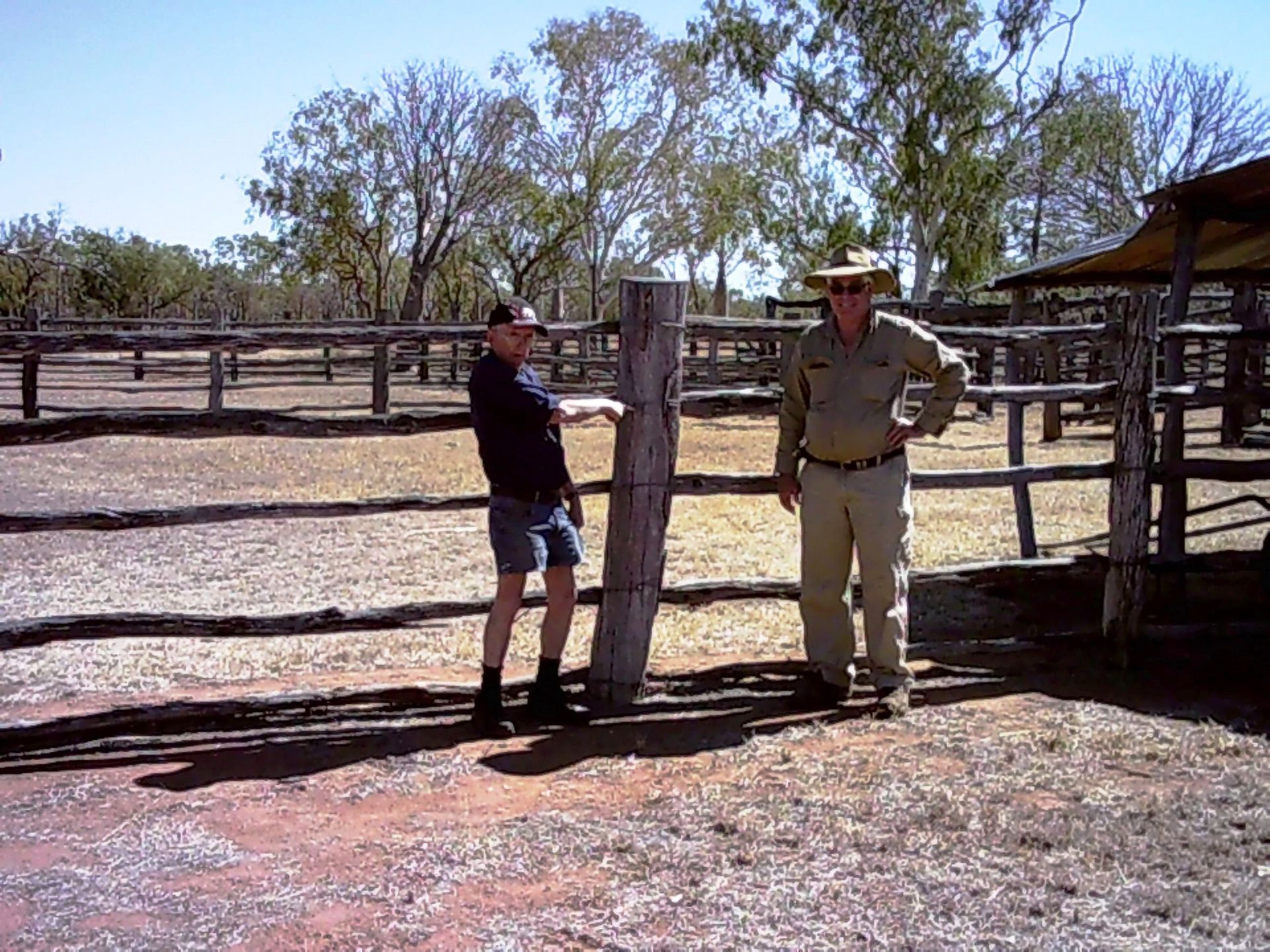 Two men standing next to a wooden fence in a field