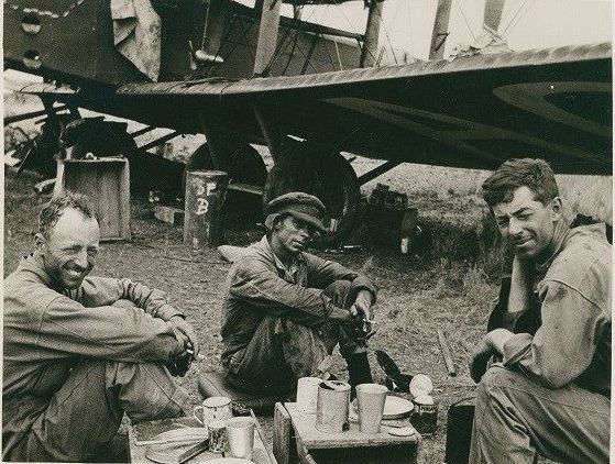 A black and white photo of three men sitting in front of a plane