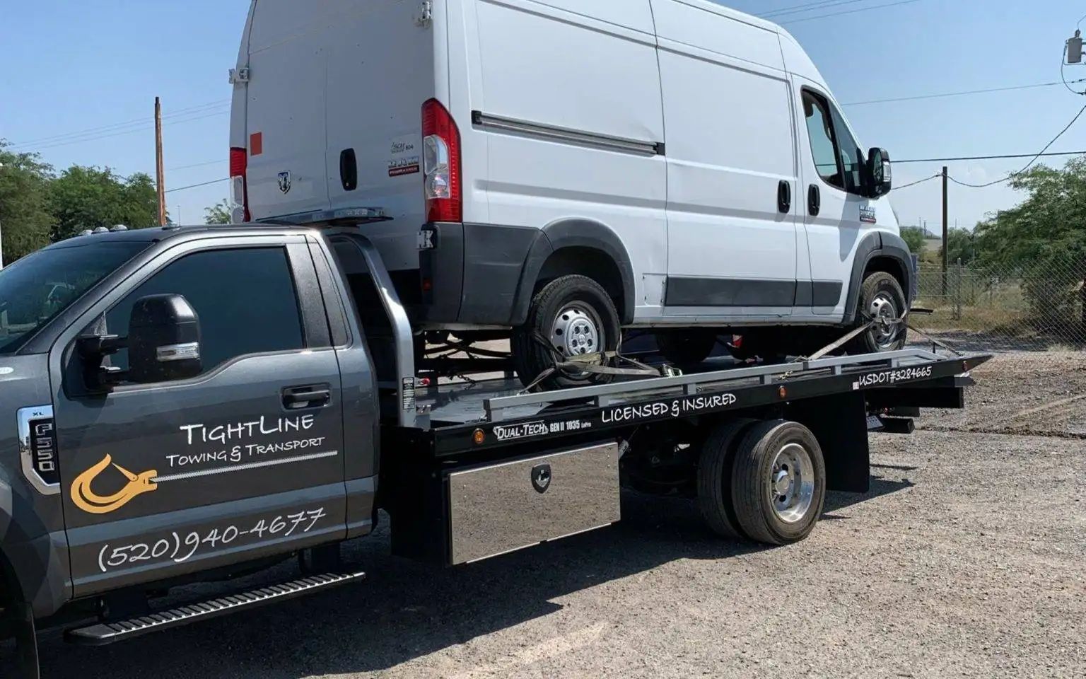 White van being towed on a flatbed truck by Tiger Line Towing. Outdoors on a sunny day.