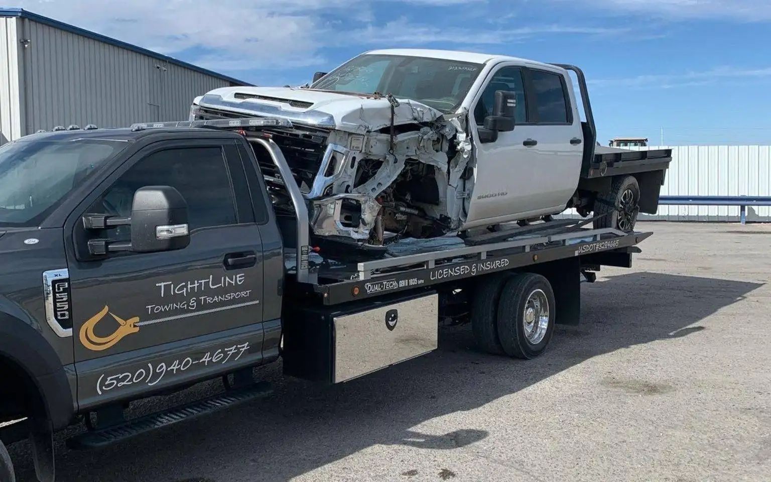 White damaged truck loaded on a flatbed tow truck. The scene is outdoors, possibly a storage yard.