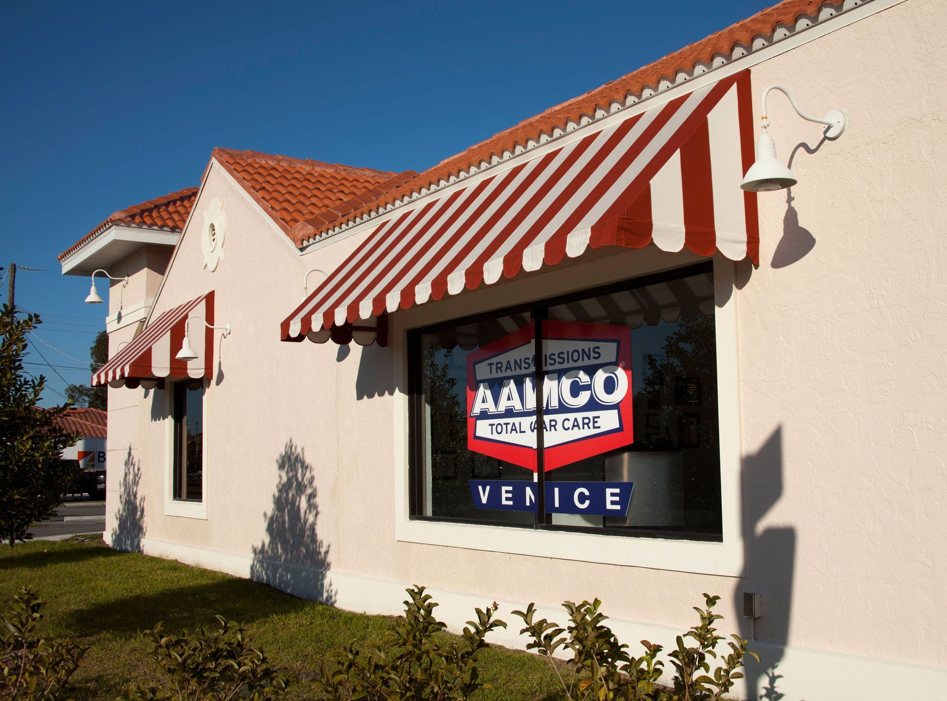 White building with red-and-white awnings and a window sign reading “AAMCO Transmissions” in Venice.