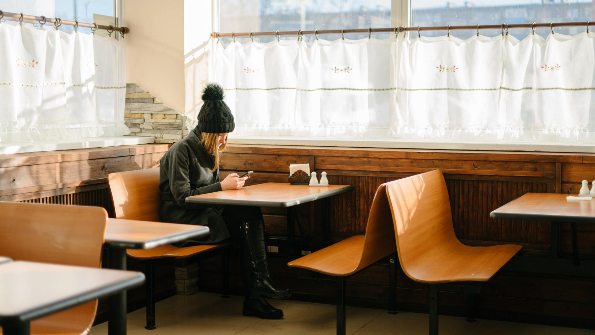 Girl sits alone in a restaurant browsing on her phone while she waits for service