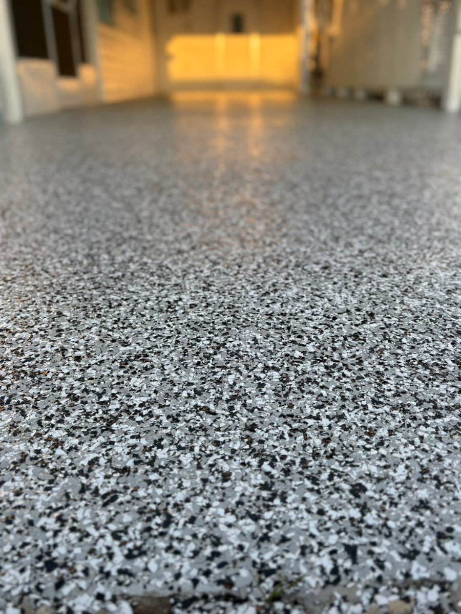 A close-up view of a floor covered in gray, black, and white decorative epoxy flakes with a glossy finish.