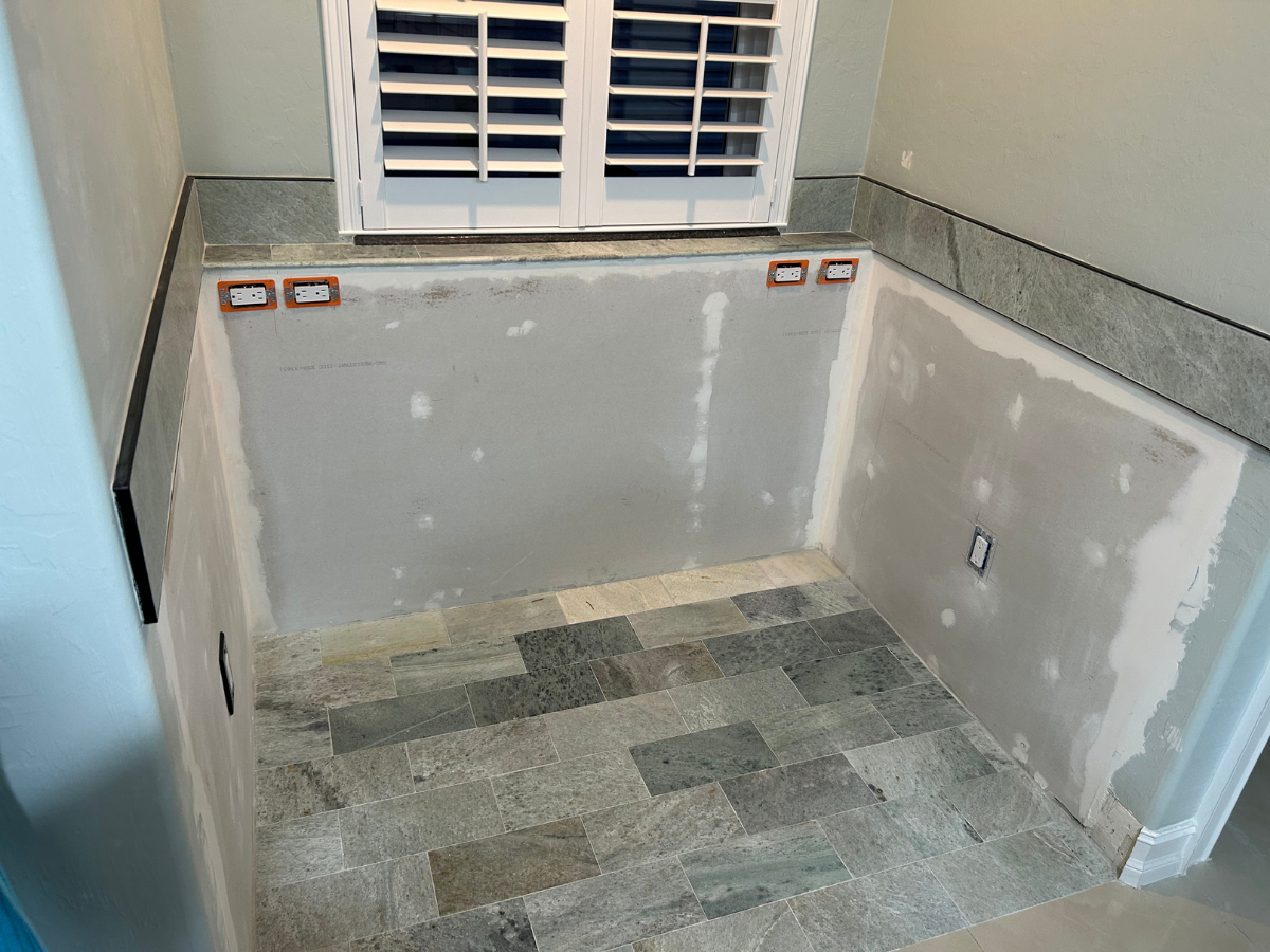 A small room alcove under a shuttered window, featuring gray stone floor tiles and partial stone wall trim.