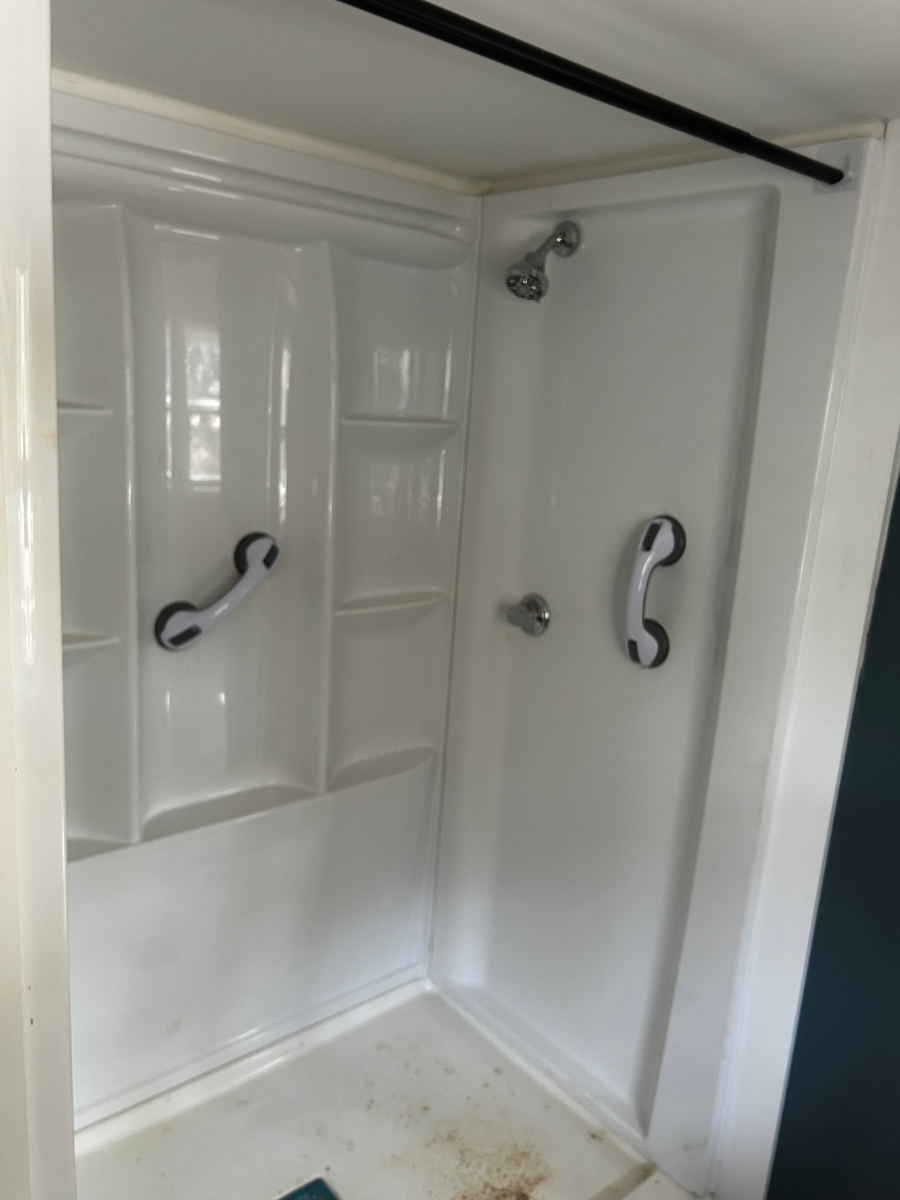 A white fiberglass shower stall featuring two suction-cup grab bars attached to the wall panels.