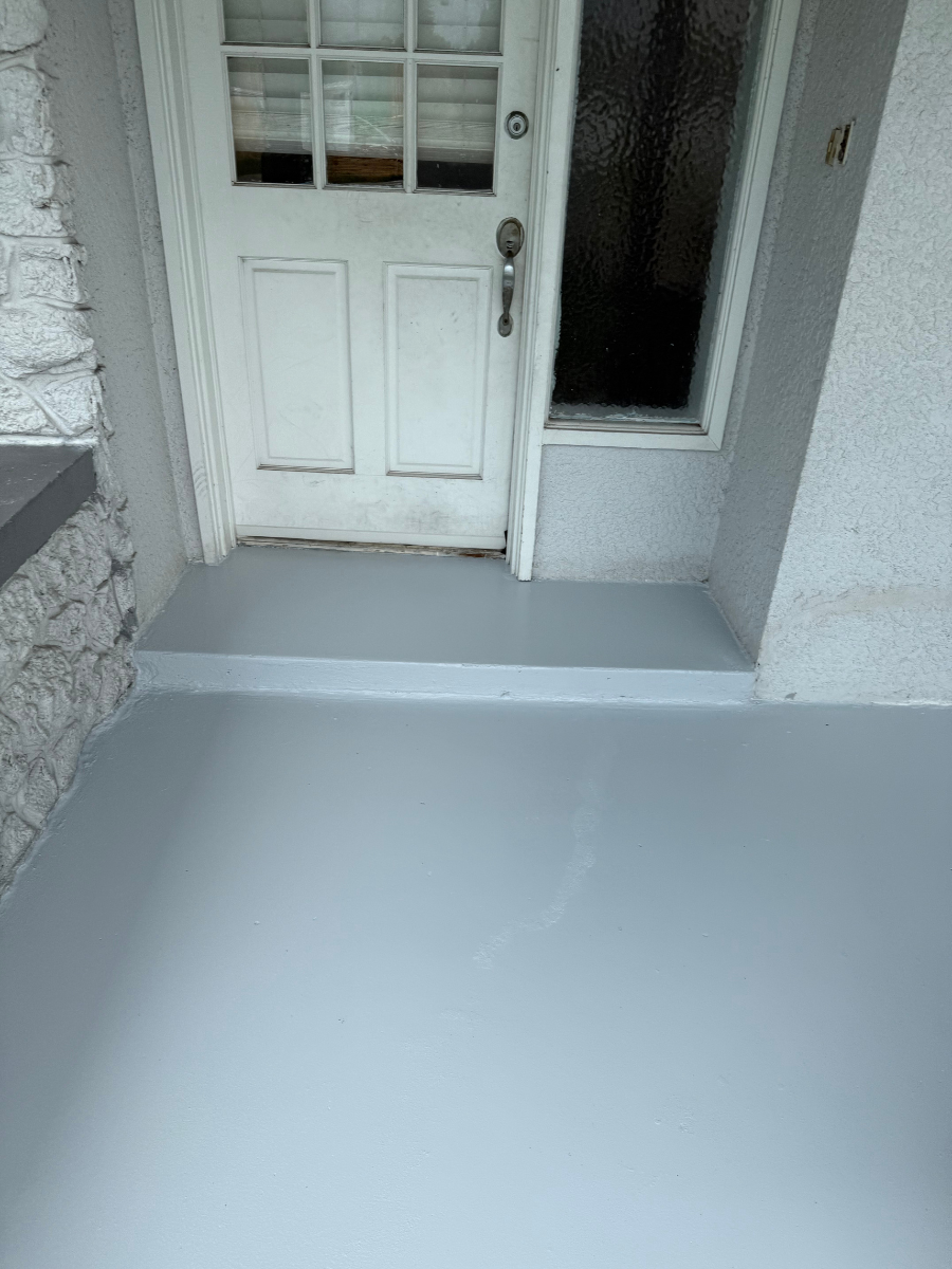 A freshly painted light gray porch leading up to a white door with a window pane.