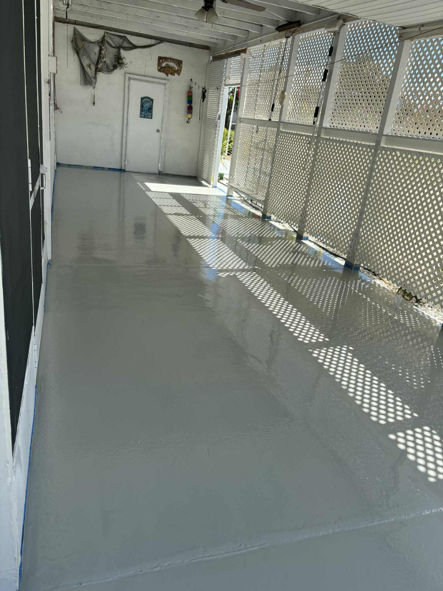 A long, covered porch with a glossy, light gray painted floor and white latticework walls on one side.