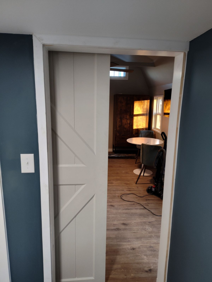 A partially open, cream-colored farmhouse-style sliding door in a doorway between dark blue walls, showing a dining area.
