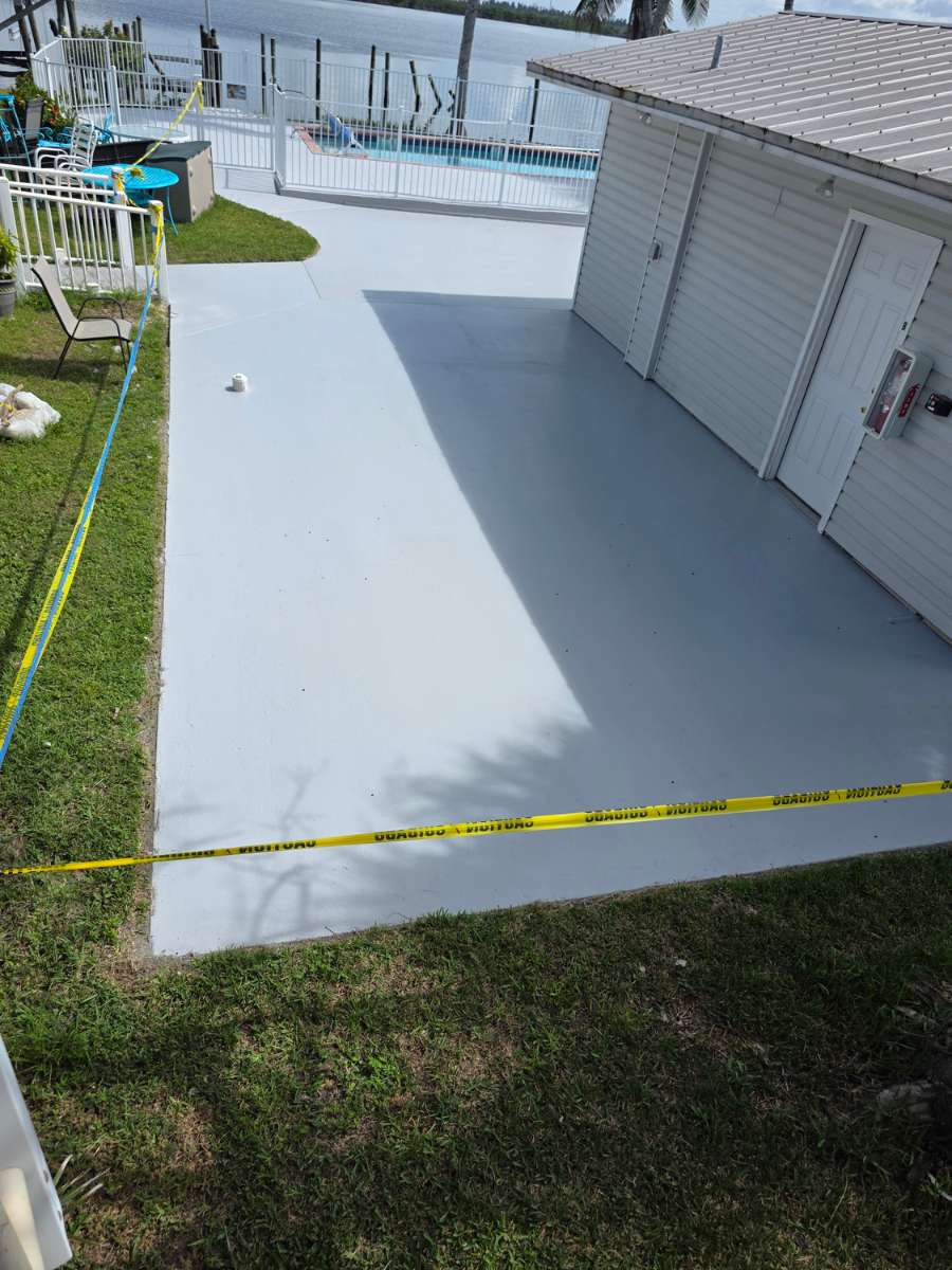 A freshly painted gray patio beside a white house, sectioned off by yellow caution tape near a waterfront.