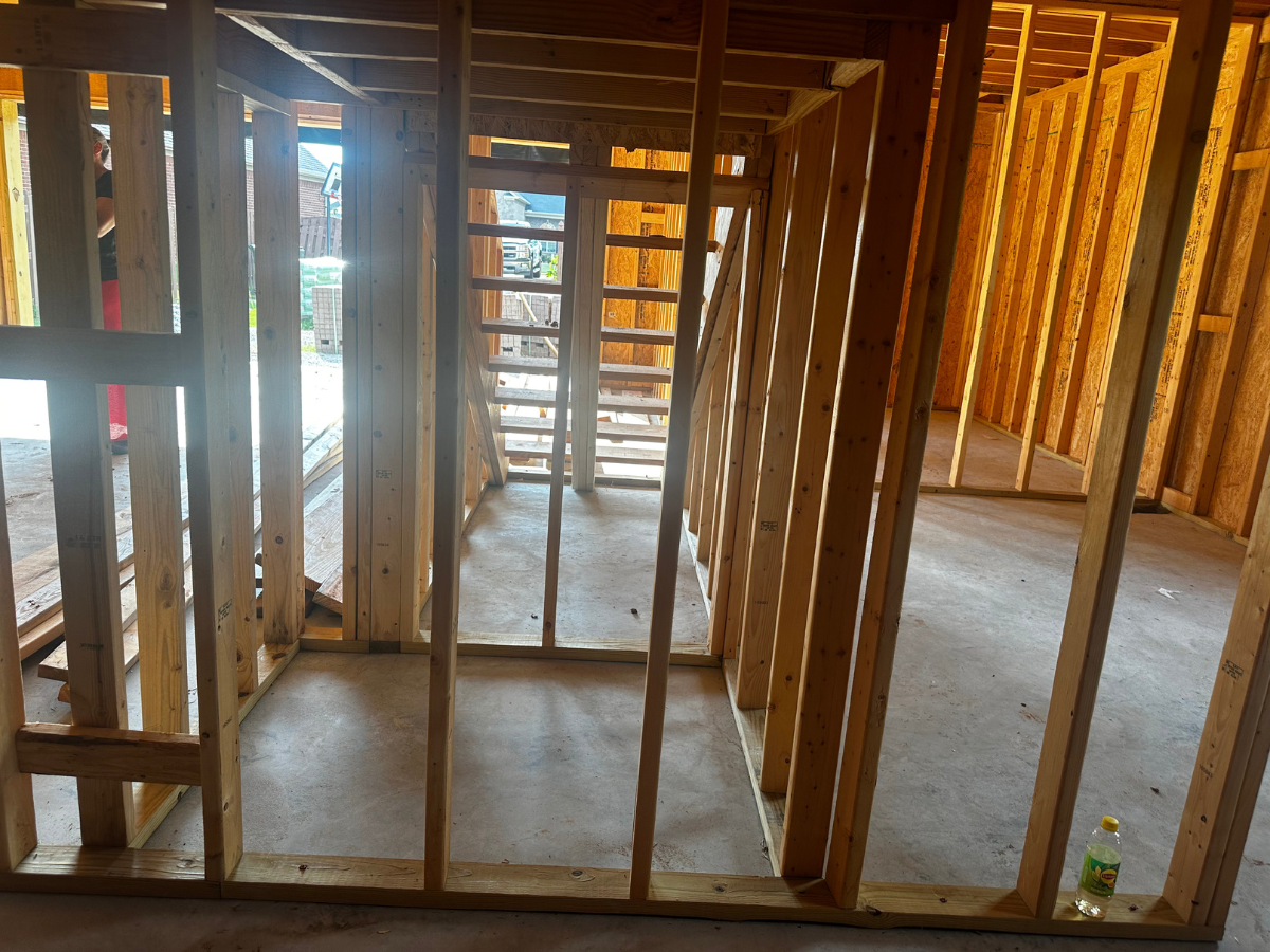 A room under construction with wooden wall framing and a partial staircase visible in the background.