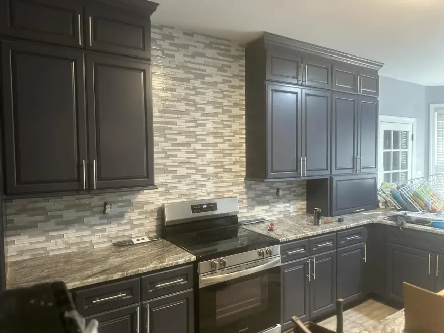 Dark blue kitchen cabinets with a stone backsplash and granite countertops.