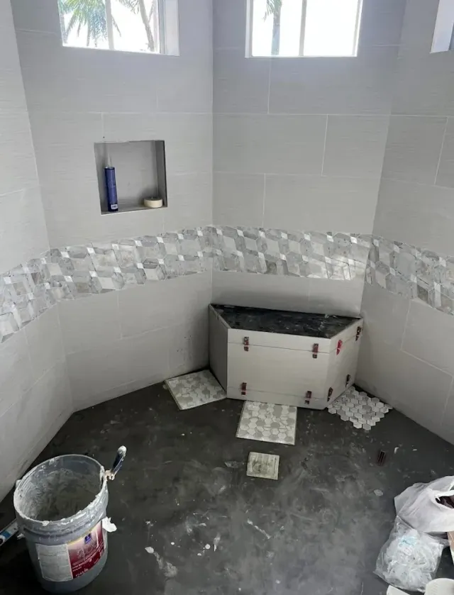 Bathroom under construction with gray and patterned tiles, gray walls, and a built-in seat.