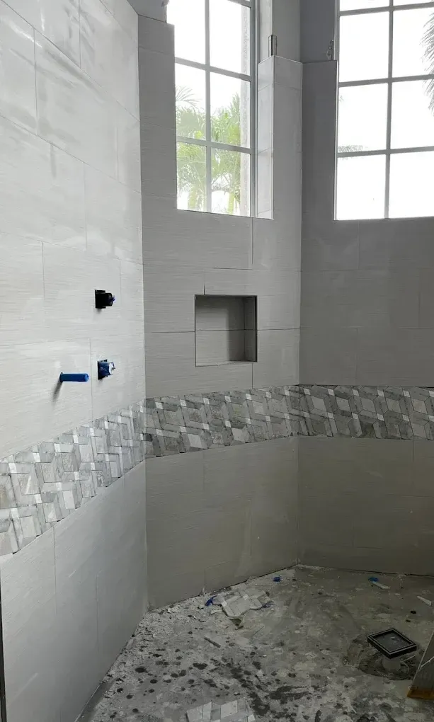 A partially tiled bathroom shower corner with a built-in niche, two windows, and plumbing fixtures installed on the wall.