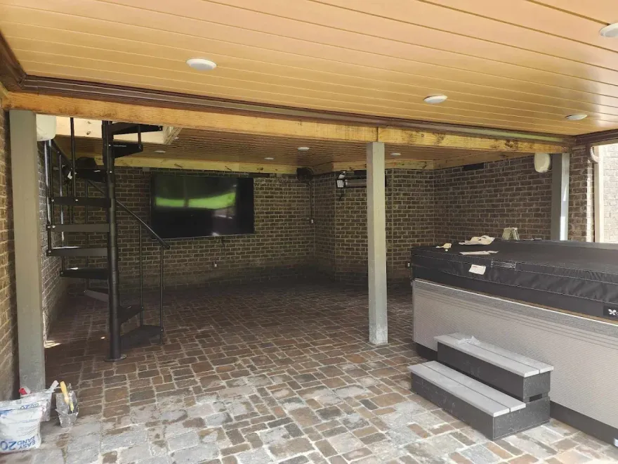 Covered outdoor space with brick floor, spiral staircase, spa, and large screen TV.