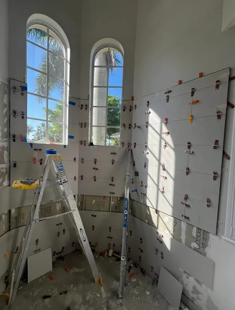 Tiling project in progress with gray tiles and leveling clips. Interior room with arched windows, a ladder, and tools.