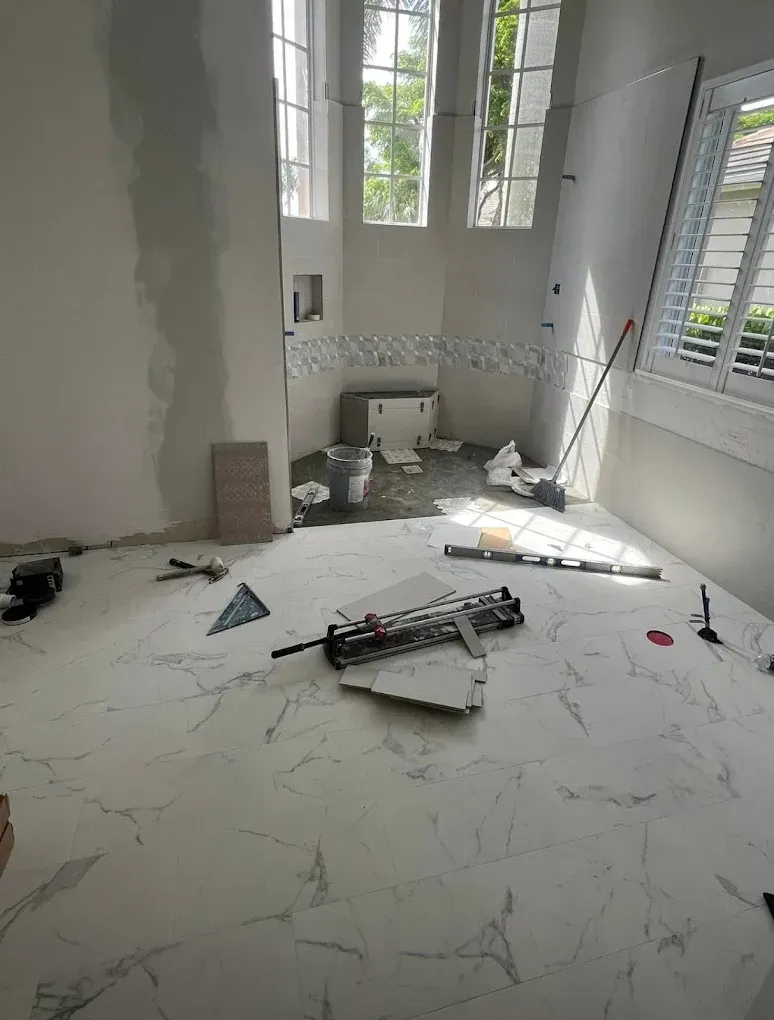 A room under renovation with white marble-patterned tile flooring, unfinished walls, tools, and a bay window.