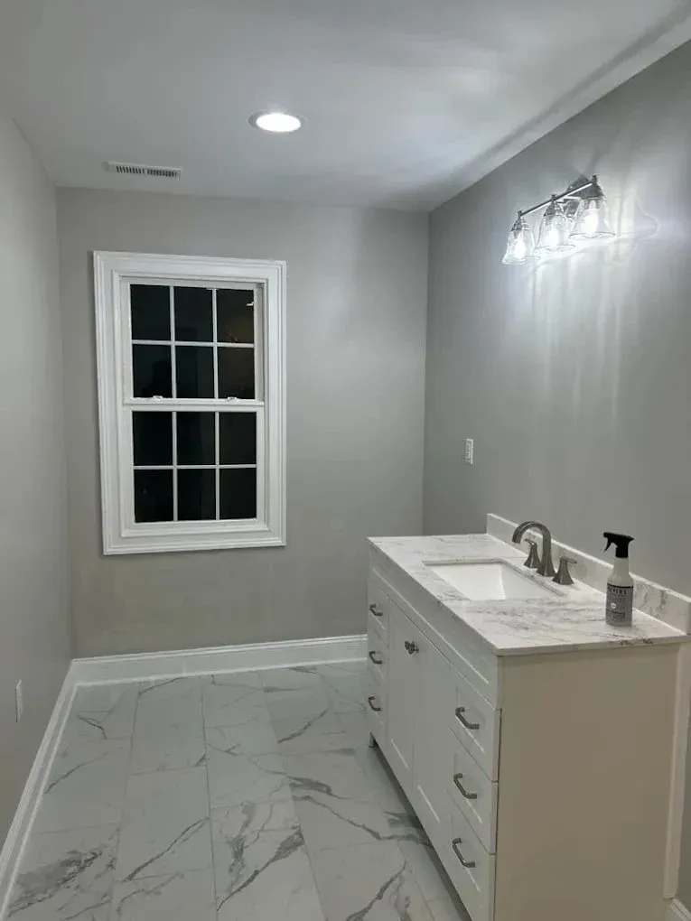 A modern bathroom with grey walls, white marble-style tiled floors, a white vanity cabinet, and a window.