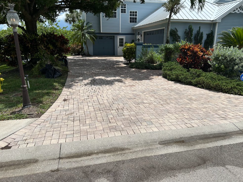 A paved driveway leads to a light blue house with a two-car garage, surrounded by landscaping and a lamppost.
