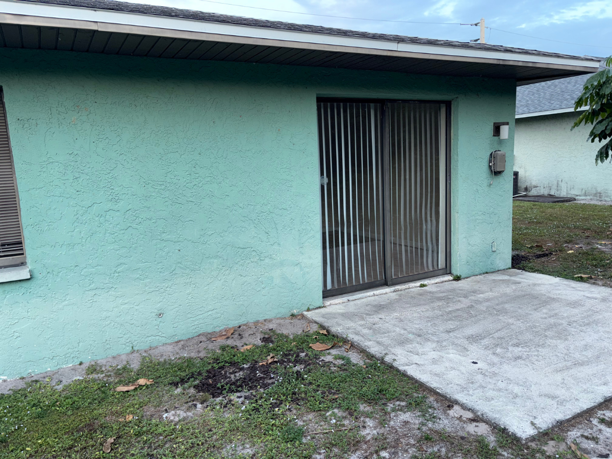 A turquoise house exterior with a sliding glass door covered by vertical blinds and a concrete patio.