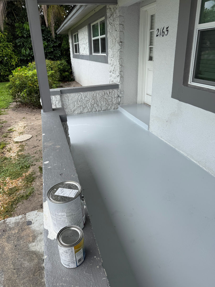 A freshly painted light gray porch at a house entrance with two paint cans sitting on a dark gray concrete ledge.